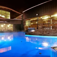 Nocą hotel z basenami termalnymi kusi błękitnym blaskiem wody i parą unoszącą się nad taflą.