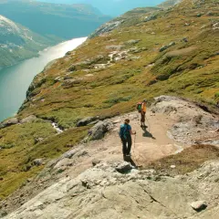 Dwie osoby wędrują po skalistym szlaku w górach w Norwegii, podziwiając malowniczy fiord.