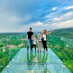 Rodzina na szklanym tarasie Sky Walk Świeradów Zdrój, podziwiająca malowniczy widok na góry i miasteczko.