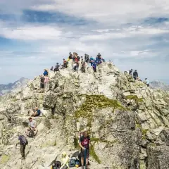 Tłum turystów na skalistym szczycie Rysów, najwyższego szczytu w Polsce. Widok na Tatry.