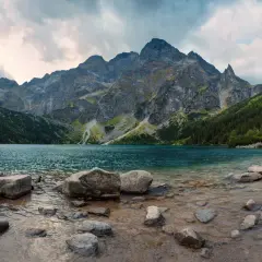 Spokojne jezioro otoczone stromymi górami i lasami. Widok na malownicze doliny w Tatrach, z kamienistym brzegiem.