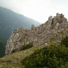 Sarnia skała wznosi się dumnie, otoczona zielenią. Na szczycie widać ludzi podziwiających panoramę.