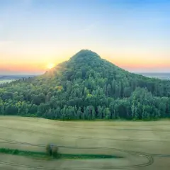 Góry Kaczawskie o wschodzie słońca. Stożkowaty, zalesiony szczyt góruje nad polami.