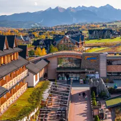 Drewniany hotel z pięknym widokiem na jesienne Tatry. W oddali widać góry i kolorowe drzewa.