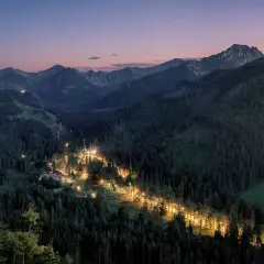 Nocny widok na Tatry, gdzie oświetlona droga tworzy świetlistą wstęgę w gęstym lesie. Zapora pod Nosalem nocą.