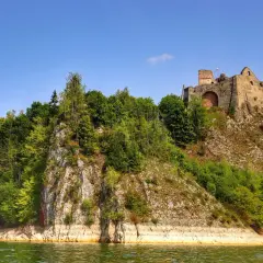 Ruiny zamku na wzgórzu nad zieloną wodą. Jezioro Czorsztyńskie w słoneczny dzień, z bujną zielenią porastającą zbocza.