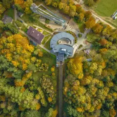 Widok z lotu ptaka na górę parkową jesienią. Widać tory kolejki, budynki i tor saneczkowy otoczone kolorowymi drzewami.