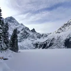 Morskie Oko zimą. Zamrożone jezioro otoczone ośnieżonymi szczytami i gęstym lasem świerkowym.
