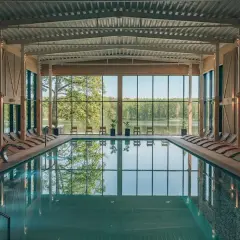 Basen w nowoczesnym spa z widokiem na jezioro. Drewniane leżaki i przeszklone ściany tworzą relaksującą atmosferę, idealną dla najlepszego spa w Polsce.