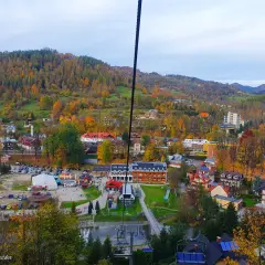 Widok z kolejki na palenice na jesienną dolinę pełną kolorowych drzew i zabudowań.