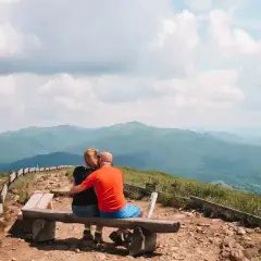 Para zakochanych na ławce podziwia bezkresne, zielone połoniny. Bieszczady jakie to góry – łagodne, rozległe, pełne spokoju.
