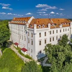 Biały zamek z czerwonym dachem, otoczony zielenią, to jeden z urokliwych zamków hoteli w Polsce.