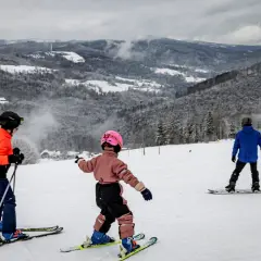 Dzieci na nartach i snowboardzie cieszą się zimowymi atrakcjami. Wspaniałe widoki górskie i śnieg zachęcają do aktywnego wypoczynku. Ferie 2026 lubuskie to idealny czas na takie przygody.