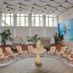 Wnętrze z piaskiem, leżakami i fontanną, ozdobione tropikalnym muralem. Idealne miejsce na relaks, to sanatorium godne polecenia.