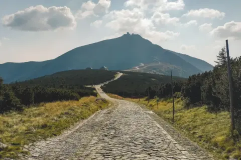 Kamienista droga prowadzi ku Śnieżce, najwyższej z gór w Karkonoszach, widocznej w oddali.