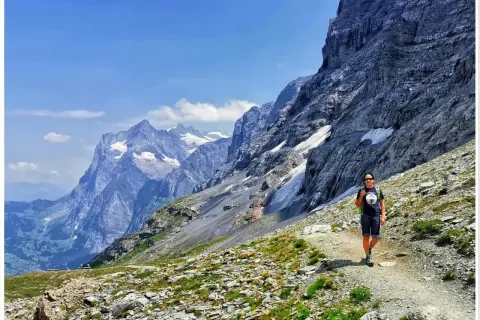 Wspaniały dzień na trekking w Alpach. Osoba z plecakiem idzie ścieżką wśród skalistych zboczy i ośnieżonych szczytów.