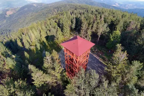 Drewniana wieża widokowa w Beskidzie Sądeckim, otoczona gęstym lasem iglastym, zaprasza do podziwiania panoramy.