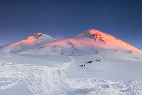 Śnieżne szczyty najwyższego wulkanu w Europie, Elbrusu, skąpane w różowym blasku wschodzącego słońca.