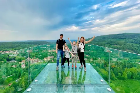 Rodzina na szklanym tarasie Sky Walk Świeradów Zdrój, podziwiająca malowniczy widok na góry i miasteczko.