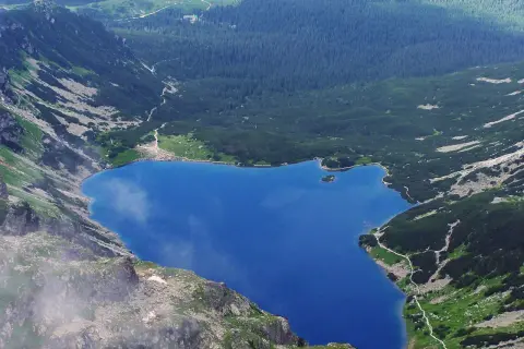 Górski, błękitny czarny staw gąsienicowy otoczony zielonymi zboczami i lasem.