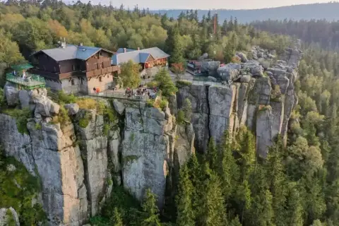 Góry Stołowe, gdzie schronisko góruje nad skalnymi urwiskami. Ludzie odpoczywają na tarasach, podziwiając widok.