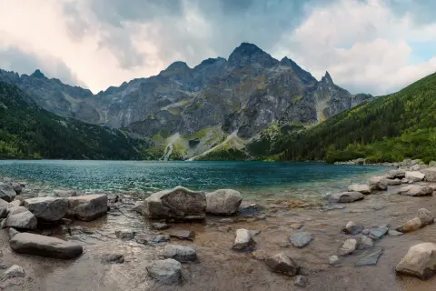 Spokojne jezioro otoczone stromymi górami i lasami. Widok na malownicze doliny w Tatrach, z kamienistym brzegiem.