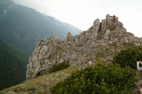 Sarnia skała wznosi się dumnie, otoczona zielenią. Na szczycie widać ludzi podziwiających panoramę.