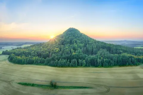 Góry Kaczawskie o wschodzie słońca. Stożkowaty, zalesiony szczyt góruje nad polami.