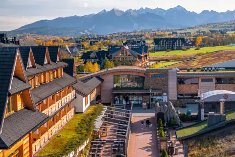 Drewniany hotel z pięknym widokiem na jesienne Tatry. W oddali widać góry i kolorowe drzewa.