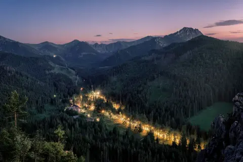 Nocny widok na Tatry, gdzie oświetlona droga tworzy świetlistą wstęgę w gęstym lesie. Zapora pod Nosalem nocą.