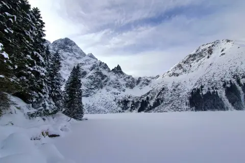 Morskie Oko zimą. Zamrożone jezioro otoczone ośnieżonymi szczytami i gęstym lasem świerkowym.