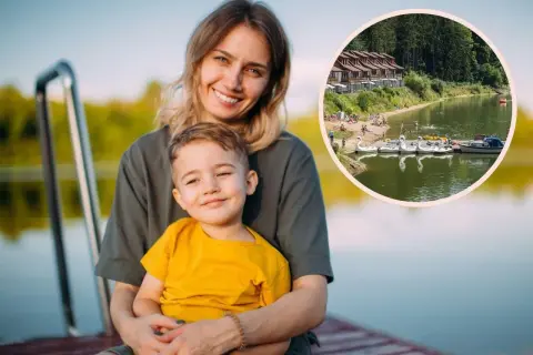Uśmiechnięta mama z synkiem na pomoście, w tle jezioro z łódkami i domkami. Idealne miejsce na wakacje z bonem turystycznym.