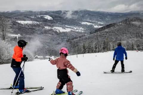 Dzieci na nartach i snowboardzie cieszą się zimowymi atrakcjami. Wspaniałe widoki górskie i śnieg zachęcają do aktywnego wypoczynku. Ferie 2026 lubuskie to idealny czas na takie przygody.