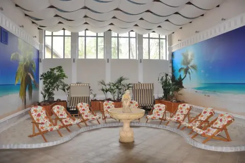 Wnętrze z piaskiem, leżakami i fontanną, ozdobione tropikalnym muralem. Idealne miejsce na relaks, to sanatorium godne polecenia.