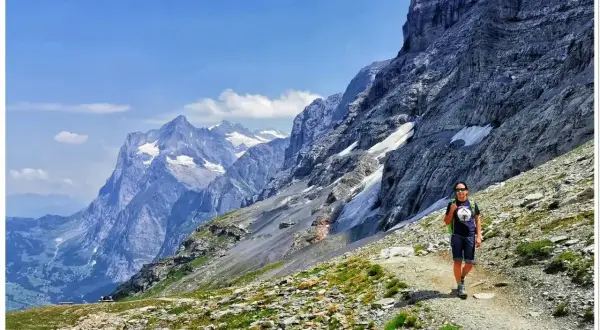 Wspaniały dzień na trekking w Alpach. Osoba z plecakiem idzie ścieżką wśród skalistych zboczy i ośnieżonych szczytów.