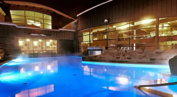 Nocą hotel z basenami termalnymi kusi błękitnym blaskiem wody i parą unoszącą się nad taflą.