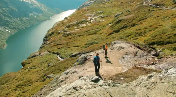 Dwie osoby wędrują po skalistym szlaku w górach w Norwegii, podziwiając malowniczy fiord.