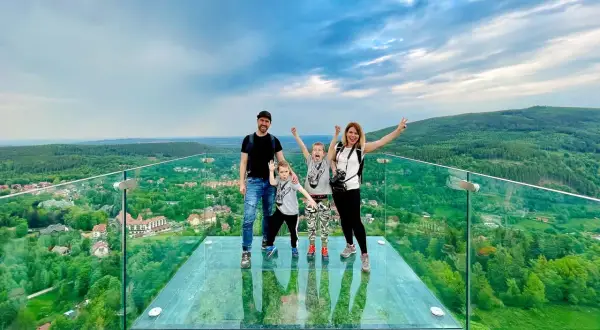 Rodzina na szklanym tarasie Sky Walk Świeradów Zdrój, podziwiająca malowniczy widok na góry i miasteczko.
