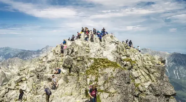 Tłum turystów na skalistym szczycie Rysów, najwyższego szczytu w Polsce. Widok na Tatry.