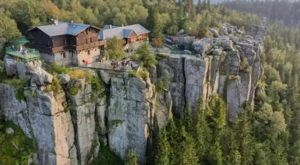 Góry Stołowe, gdzie schronisko góruje nad skalnymi urwiskami. Ludzie odpoczywają na tarasach, podziwiając widok.