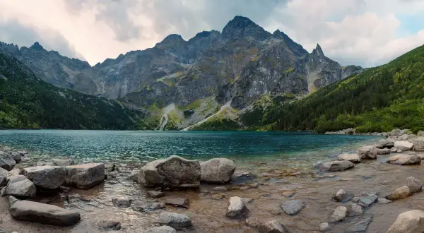 Spokojne jezioro otoczone stromymi górami i lasami. Widok na malownicze doliny w Tatrach, z kamienistym brzegiem.