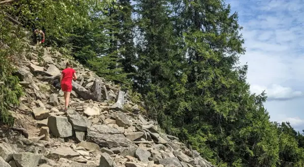 Dziewczyna w czerwonej sukience wspina się po kamienistym zboczu w lesie. Widok na Luboń Wielki.