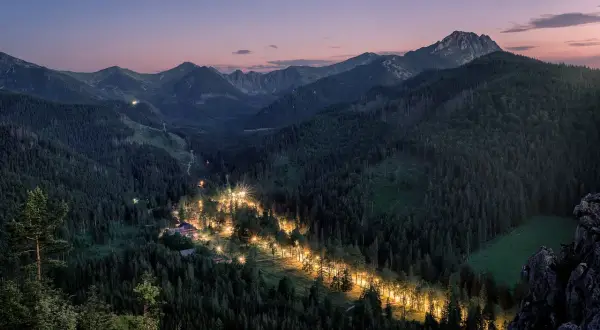 Nocny widok na Tatry, gdzie oświetlona droga tworzy świetlistą wstęgę w gęstym lesie. Zapora pod Nosalem nocą.