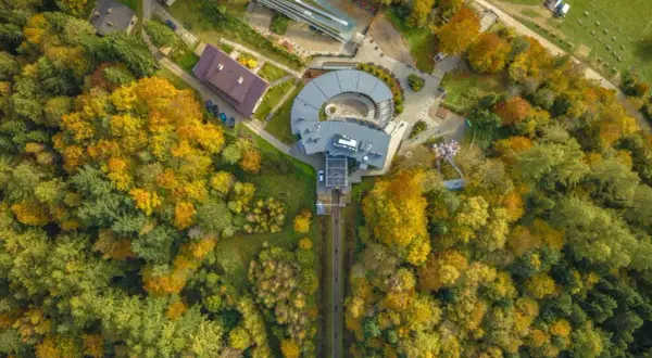Widok z lotu ptaka na górę parkową jesienią. Widać tory kolejki, budynki i tor saneczkowy otoczone kolorowymi drzewami.