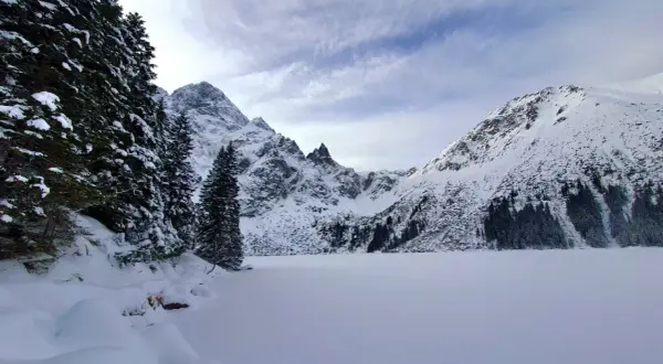 Morskie Oko zimą. Zamrożone jezioro otoczone ośnieżonymi szczytami i gęstym lasem świerkowym.
