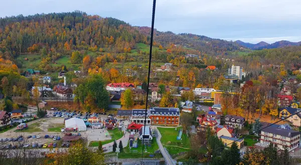 Widok z kolejki na palenice na jesienną dolinę pełną kolorowych drzew i zabudowań.