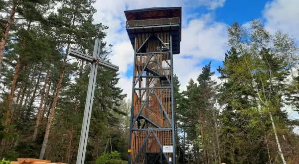 Skiełek wieża widokowa w otoczeniu lasu, obok metalowy krzyż i drewniane ławki.