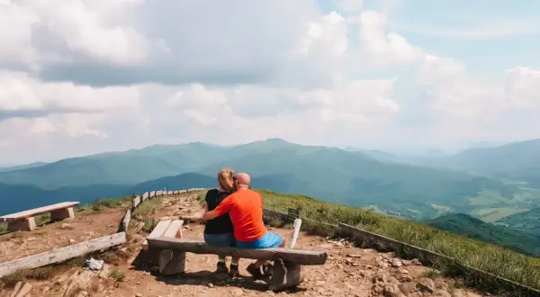Para zakochanych na ławce podziwia bezkresne, zielone połoniny. Bieszczady jakie to góry – łagodne, rozległe, pełne spokoju.