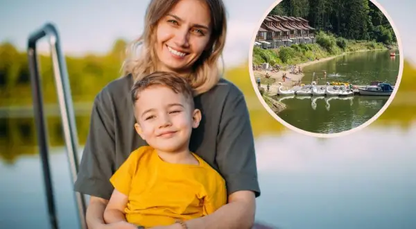 Uśmiechnięta mama z synkiem na pomoście, w tle jezioro z łódkami i domkami. Idealne miejsce na wakacje z bonem turystycznym.