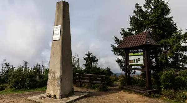 Pomnik na Turbaczu, najwyższym szczycie Gorców, z tablicą informacyjną i ławką.